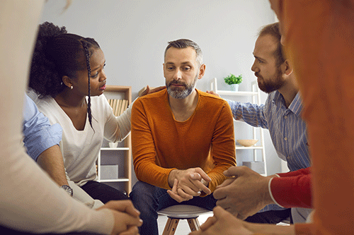 a group of people put hands on the shoulders of a man in alcohol addiction treatment