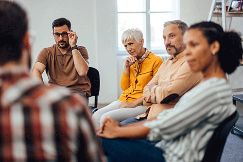 group of mature men and women listening intently as part of a group therapy session at a benzo addiction center