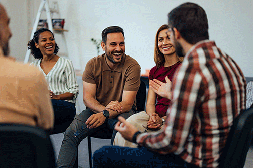 smiling men and women seated in a circle and engaging as part of group therapy for addiction treatment