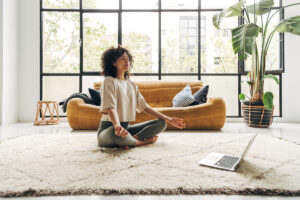 woman seated in lotus position on her floor in front of laptop demonstrating meditative therapy what it is and how it works