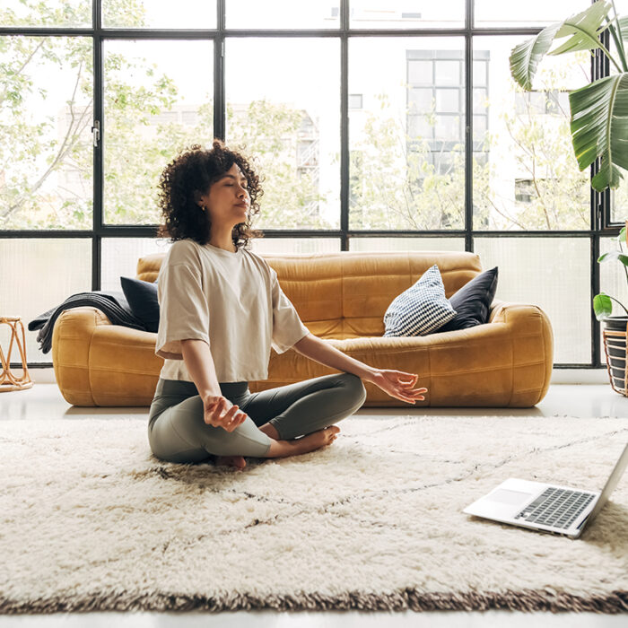 woman seated in lotus position on her floor in front of laptop demonstrating meditative therapy what it is and how it works