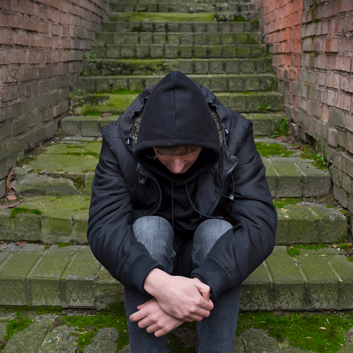 young man in hoodie with head bowed seated outside on concrete steps wondering what are 5 facts about heroin addiction