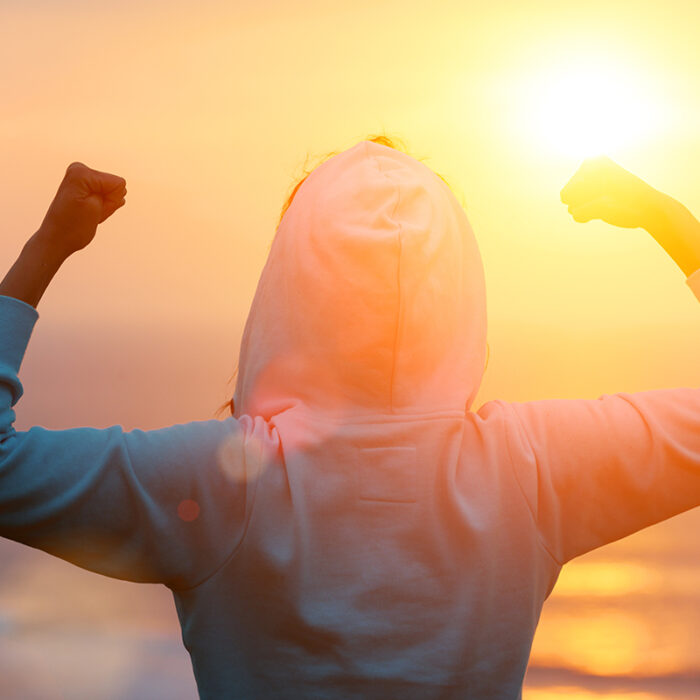 person standing on the shore facing the sunrise with arms raised realizing what are the 5 benefits of motivational enhancement therapy