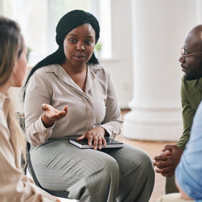 group of men and women seated in a circle and discussing what are the benefits of a a substance abuse alumni program