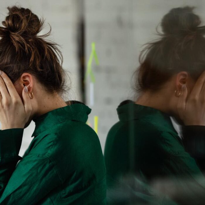 young woman leaning against bathroom mirror with head in her hands wondering what to know about opioid use disorder