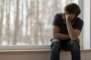 A man struggling with self-medicating for depression looks out the window.