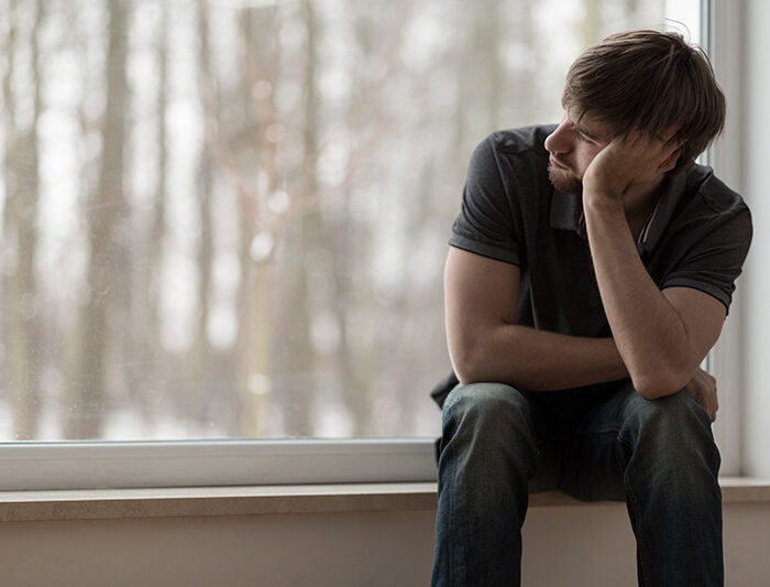 A man struggling with self-medicating for depression looks out the window.